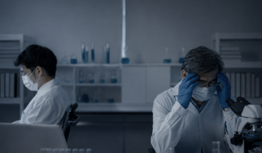 疲労感のある検査室で頭を抱える臨床検査技師